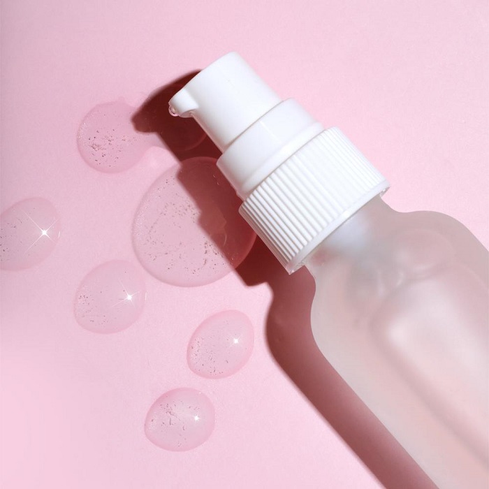 a bottle of clear face
                serum on a pink background