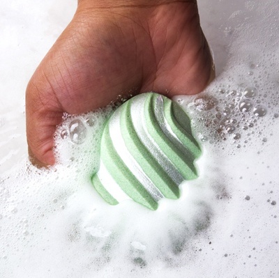 A
                bath bomb in a hand partially sumberged in water, foaming