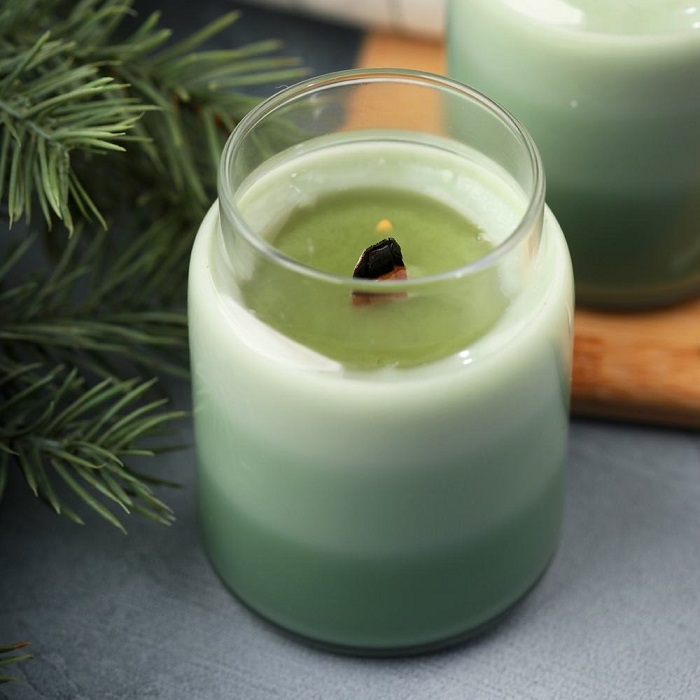 A candle layered in shades of green with a lit wooden wick