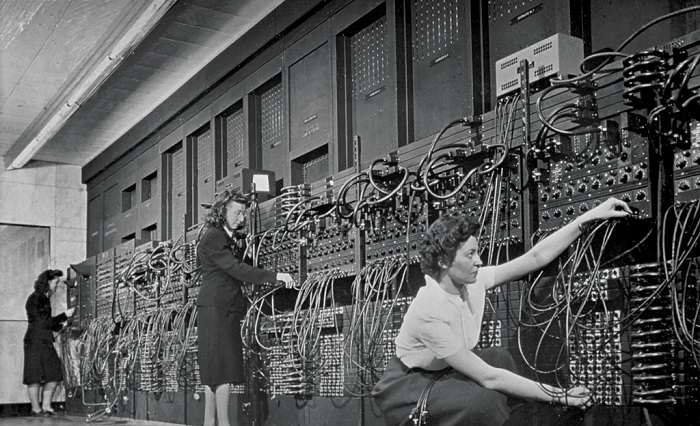 a black and white photo of a team of women
                operating a large computer